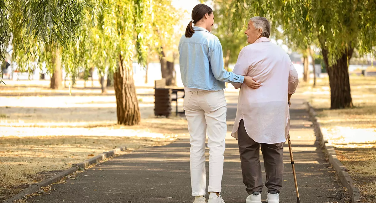 Assistante de vie accompagnant une personne âgée en promenade dans un parc